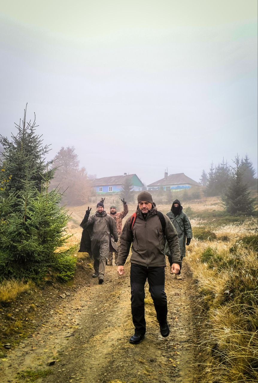 Група людей спускається гірською дорогою в тумані, позаду видно притулок серед ялин.