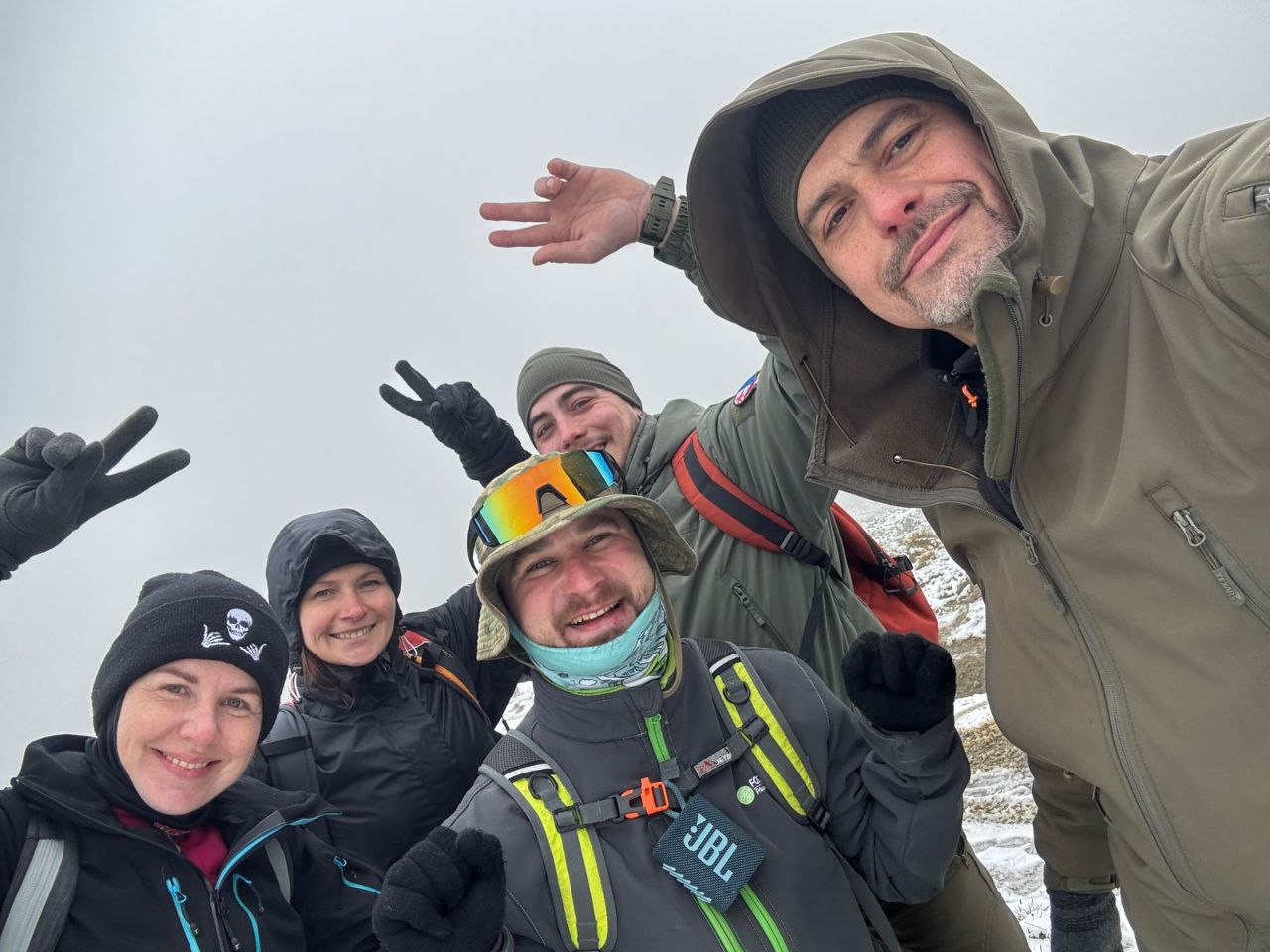 Групове фото учасників походу на гірській вершині в тумані, всі усміхаються і показують жест перемоги