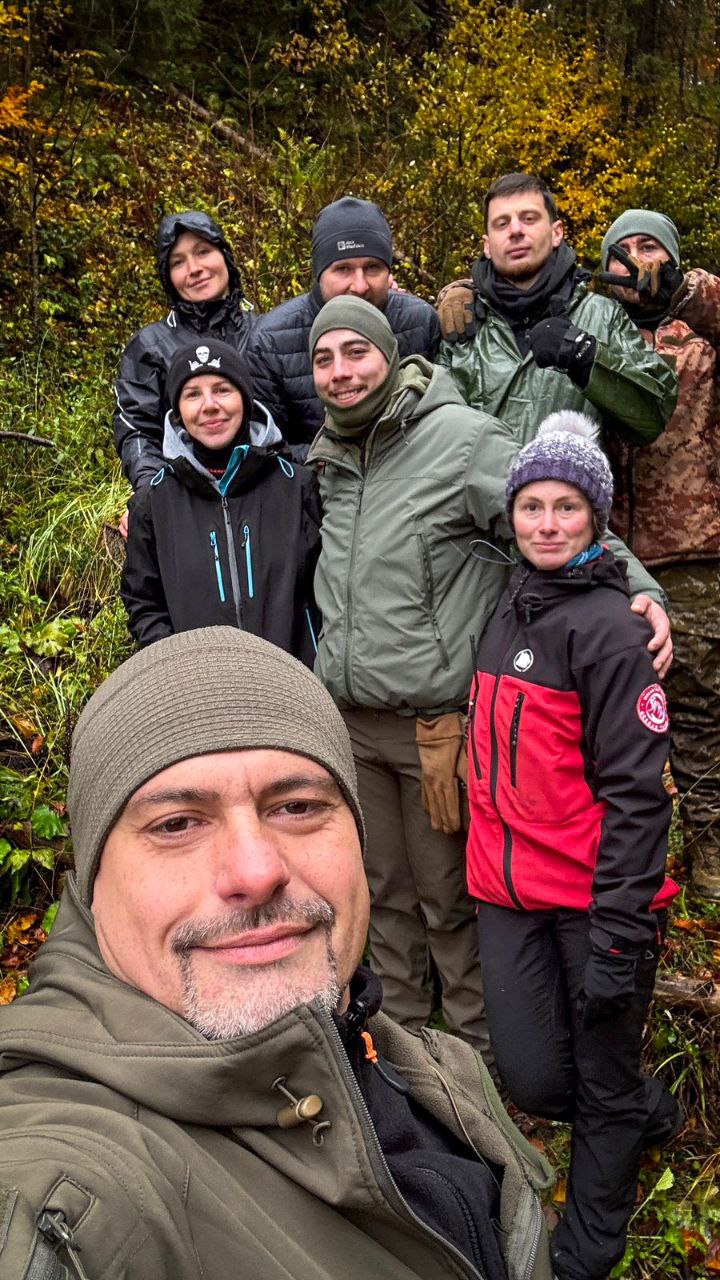 Невелика група учасників стоїть разом і усміхається, на фоні осіннього лісу.