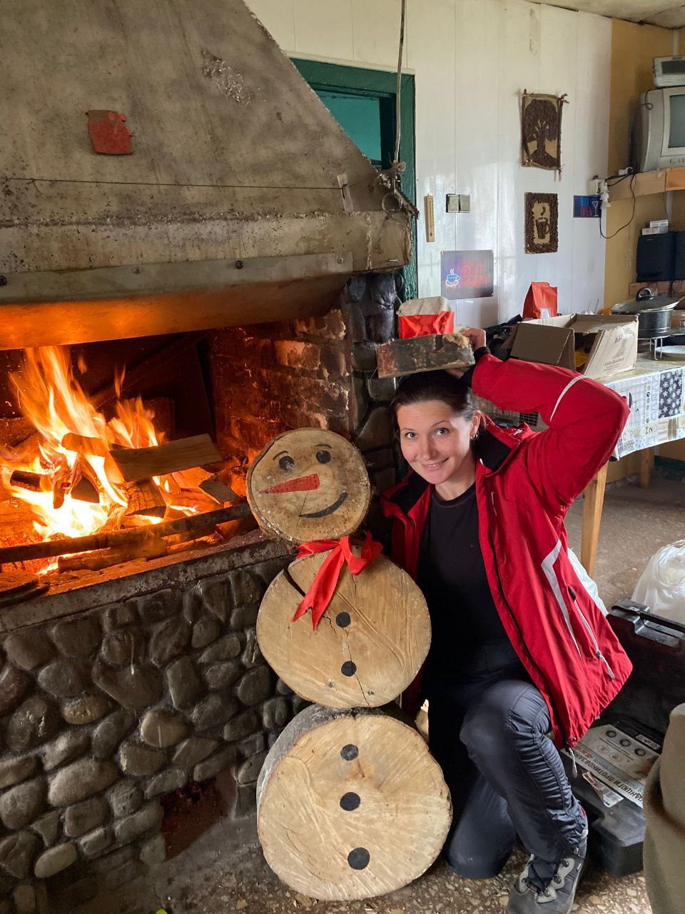 Імпровізований сніговик із дерев’яних колод біля каміна, а учасниця програми жартома тримає йому 'капелюха'