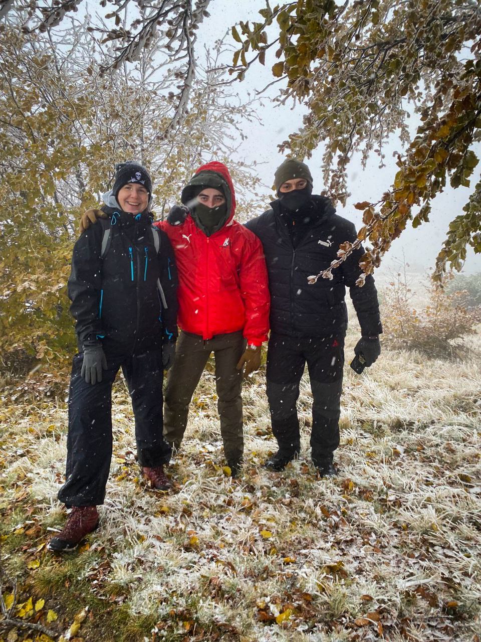 Троє людей стоять на гірській галявині під час снігопаду, на деревах видно іній.