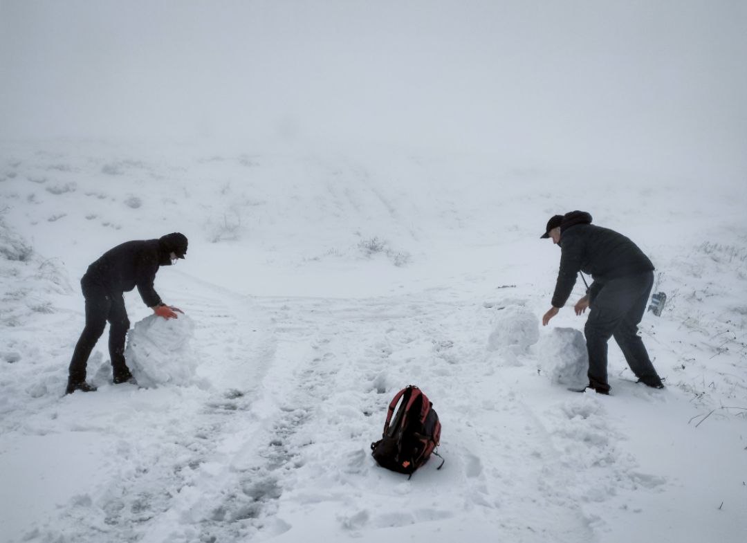 Двоє учасників ліплять снігові кулі під час снігопаду на високогір'ї. Поруч на снігу лежить рюкзак.